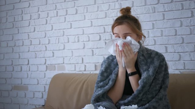 Ill upset young woman blowing running nose got flu concept caught cold sneezing in tissue sit on sofa, sick girl having health problem flue allergy symptoms coughing holding napkin alone in home