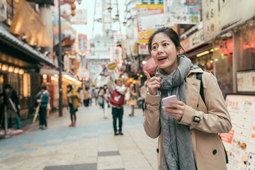 Fototapeta premium asian woman tourist holding cellphone looking online map app finding direction standing in dotonbori street in osaka japan. girl backpacker excited pointing finger to right way on teeming place.