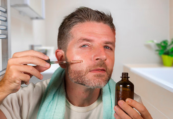 happy and attractive camp homosexual man applying moisturizer facial serum with bathroom towel...