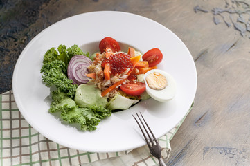 Close-up salad with crab meat, avocado, fresh vegetables and red salmon caviar on a white plate. Horizontal shot. Serving on a checkered napkin.