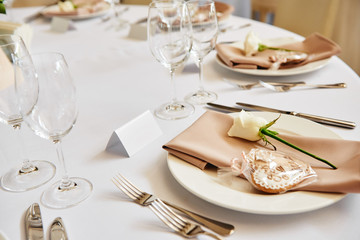 Table setting with blank guest card, white plate with beige serviette, rose, heart and cutlery on table, copy space. Place setting at wedding reception. Table served for wedding banquet in restaurant