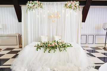 Wedding presidium in restaurant, copy space. Banquet table for newlyweds with flowers, greenery, candles and garland ligths. Lush floral arrangement. Luxury wedding decorations