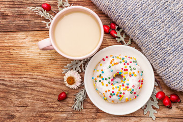 Hot coffee with a donut. Autumn drink for a good mood with plaid, fresh rose hips, leaves and flowers. Old wood plank background