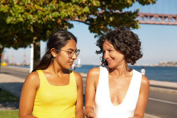 Cheerful multiethnic women walking at riverside. Beautiful smiling female friends walking and talking near river. Friendship concept