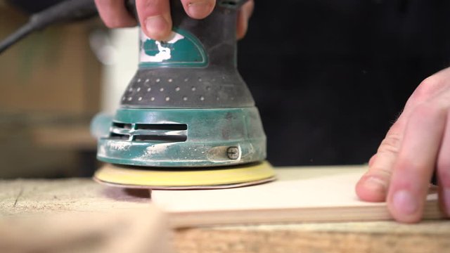 Wood sanding. Orbital sander for woodworking. Carpenter grinds a wooden product with a grinder.