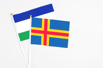 Aland Islands and Lesotho stick flags on white background. High quality fabric, miniature national flag. Peaceful global concept.White floor for copy space.