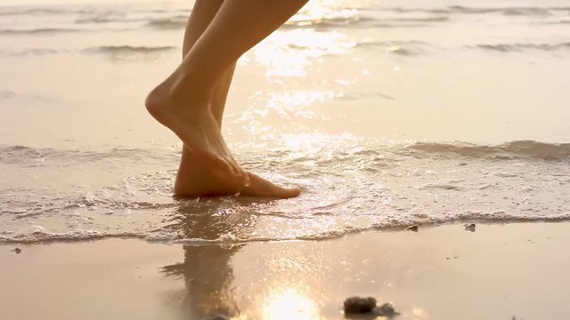 Person walking on the beach at sunset during summer vacation holidays, closeup of legs and feet in the sea water, dolly video shot 60 fps