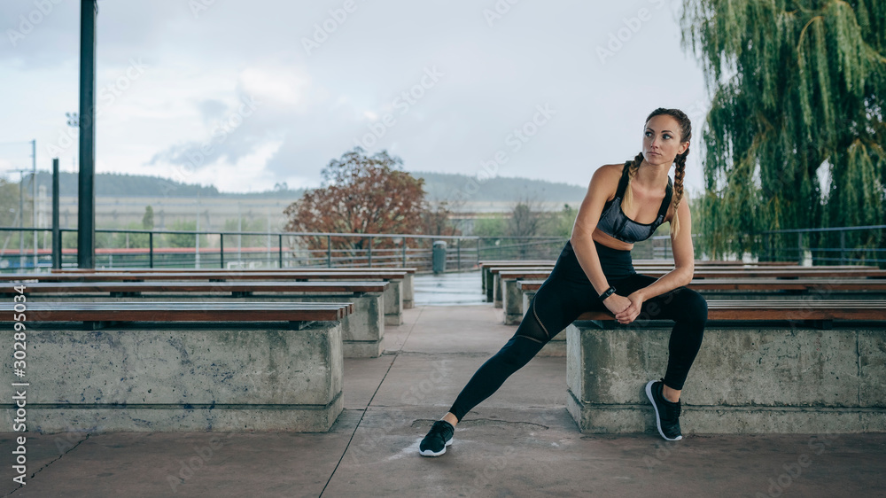 Sticker Young sportswoman posing sitting on a bench outdoors