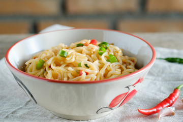 A cup of instant noodles placed on a wooden table With chilli as ingredients
