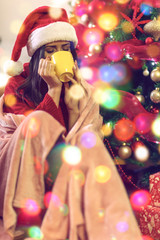 woman sitting by the christmas tree and drinking hot tea