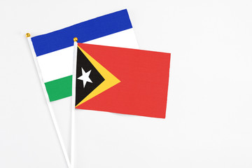 East Timor and Lesotho stick flags on white background. High quality fabric, miniature national flag. Peaceful global concept.White floor for copy space.