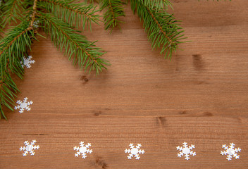 Fir branches and white snowflakes on a wooden background.