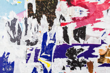 Old torn and peeling paper posters on dirty billboard texture background.