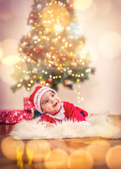 Cute baby boy in Christmas costume and gift box on floor at home