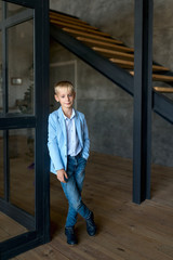 Fototapeta na wymiar The blonde teenager, in a stylish shirt and jeans, stands in a loft-style apartment and smiles broadly at the camera