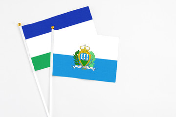 San Marino and Lesotho stick flags on white background. High quality fabric, miniature national flag. Peaceful global concept.White floor for copy space.