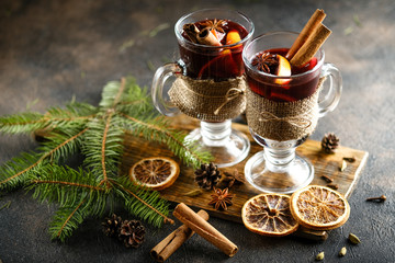 Obraz na płótnie Canvas Mulled wine in glass glasses with apples, orange, cinnamon and star anise. Hot christmas drink on dark background with spruce branch.