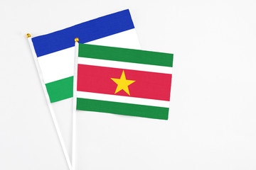 Suriname and Lesotho stick flags on white background. High quality fabric, miniature national flag. Peaceful global concept.White floor for copy space.