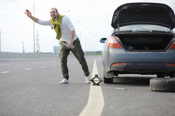 Replacing the wheel of a car on the road. A man doing tire work on the sidelines.