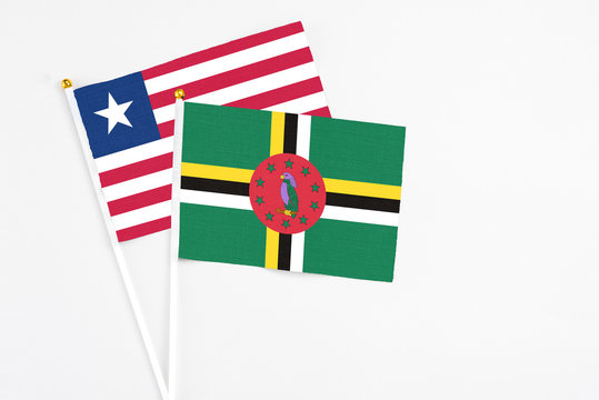 Dominica and Liberia stick flags on white background. High quality fabric, miniature national flag. Peaceful global concept.White floor for copy space.