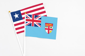 Fototapeta premium Fiji and Liberia stick flags on white background. High quality fabric, miniature national flag. Peaceful global concept.White floor for copy space.