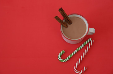 mug of hot chocolate cocoa with cinnamon and candy sugar canes on a red background with copy space for text. Flat lay. Top view. Christmas background, composition, card, pattern, poster. 