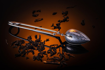 Still life tea custard spoon with reflections on the glass with an orange spot on the background and scattered tea leaves