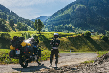 Girl in full body protection, turtle armor, knee pads and helmet, motorcycle for traveling with large luggage, on a background of green mountains, copy space, rady to ride - obrazy, fototapety, plakaty