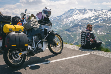 A motorcycle traveler sitting on the edge of the earth and looking into the distance. top of the mountain, Grossglockner pass, biker dressed in a protective jacket armor. Austria, motorbike with bags © Sergey