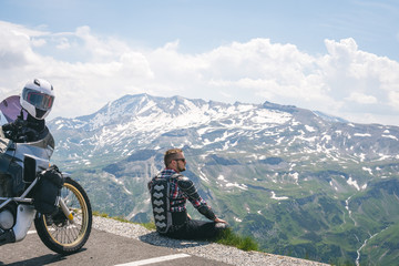 A motorcycle traveler sitting on the edge of the earth and looking into the distance. top of the mountain, Grossglockner pass, biker dressed in a protective jacket armor. Austria, copy space