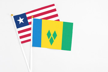 Saint Vincent And The Grenadines and Liberia stick flags on white background. High quality fabric, miniature national flag. Peaceful global concept.White floor for copy space.
