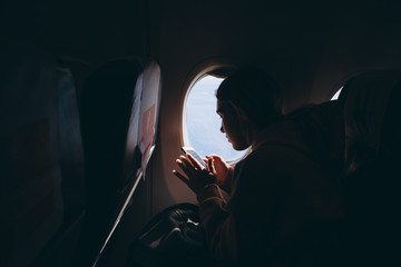 girl who flies for the first time and sits on a chair by the window enjoys the view from the...
