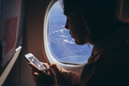 girl who flies for the first time and sits on a chair by the window enjoys the view from the window, takes pictures, is happy about her first flight on the plane, selective focus, noise effect