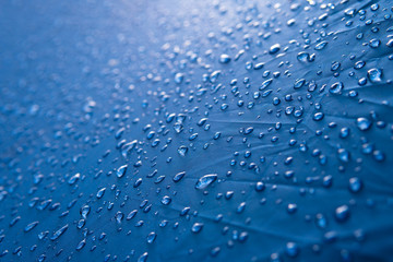 Water drops on waterproof nylon fabric. Macro detail view of texture of blue woven synthetic...
