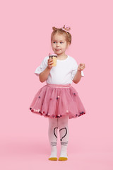 Cute child girl with pleasure eats tasty ice-cream on a pink studio background. Licks with closed eyes. The concept of baby food and a happy childhood