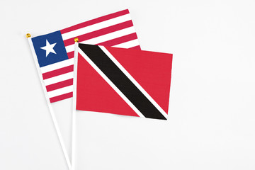 Trinidad And Tobago and Liberia stick flags on white background. High quality fabric, miniature national flag. Peaceful global concept.White floor for copy space.