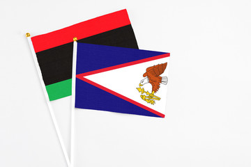 American Samoa and Libya stick flags on white background. High quality fabric, miniature national flag. Peaceful global concept.White floor for copy space.
