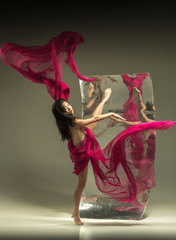 Dance with fire. Modern ballet dancer on brown background with mirror. Illusion reflections on surface. Magic of flexibility, motion with fabric. Concept of creative art dancing, action, inspiring.