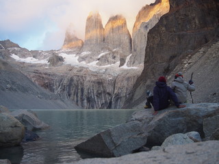 A couple sits on a rock and gazes at the majestic sunlit mountain Torres del Paine, Amazing...