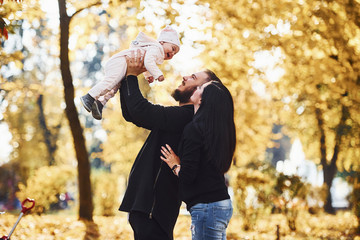 Cheerful family having fun together with their child in beautiful autumn park