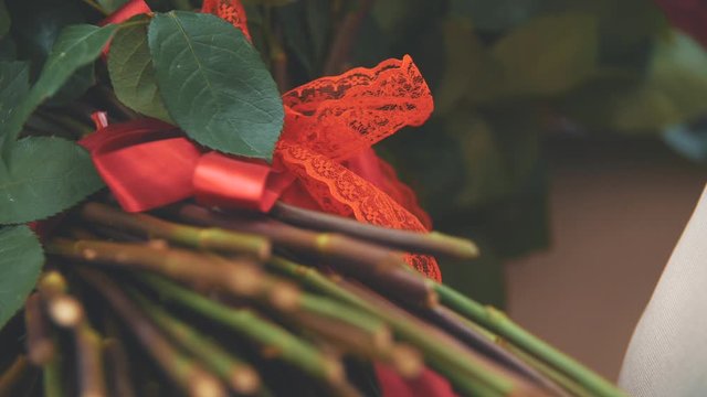 Cropped video of bouquet of large red roses. Focus on the red ribbon tied in nice knot.