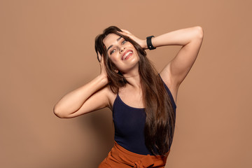 Freestyle. Young girl in top standing studio isolated on brown holding head posing to camera cheerful