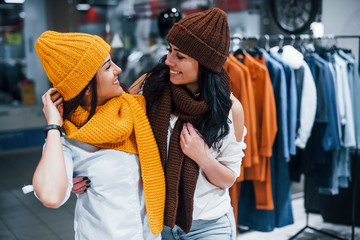 Trying warm hats and scarfs. Two young women have a shopping day together in the supermarket