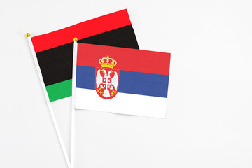 Serbia and Libya stick flags on white background. High quality fabric, miniature national flag. Peaceful global concept.White floor for copy space.