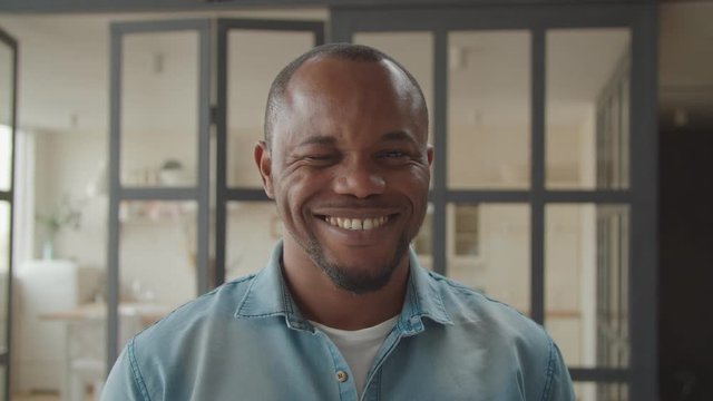 Portrait of friendly excited handsome african guy posing with cheerful toothy smile and winking playfully indoors, expressing carefree mood, positivity and flirt.