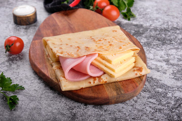 Delicious pancakes with ham and cheese on wooden board, concrete gray stone table background. Top...