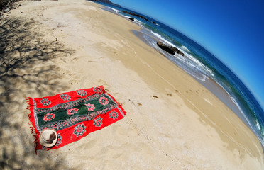Wide-angle view of beautiful beach. Shadows of tree on sand. Towel, hat and foot prints going to water. Wide angle fish-eye lens used to enhance panoramic effect.