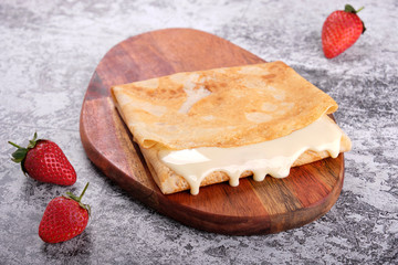 Delicious pancakes with condensed milk, sweet sauce on wooden board, concrete gray stone table background. Top view homemade breakfast. Russian national food. Russian cuisine.