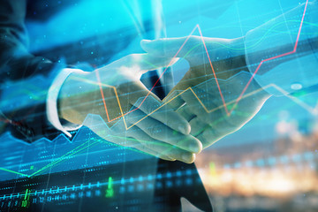 Double exposure of financial chart on cityscape background with two businessmen handshake. Concept of financial analysis and investment opportunities