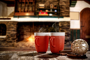 Christmas mugs with a hot drink. Steam smoke and Christmas decoration. Blurry background of a rustic fireplace with flame. American rifles on a stand. Place for your christmas gifts.Dark mood shadows.